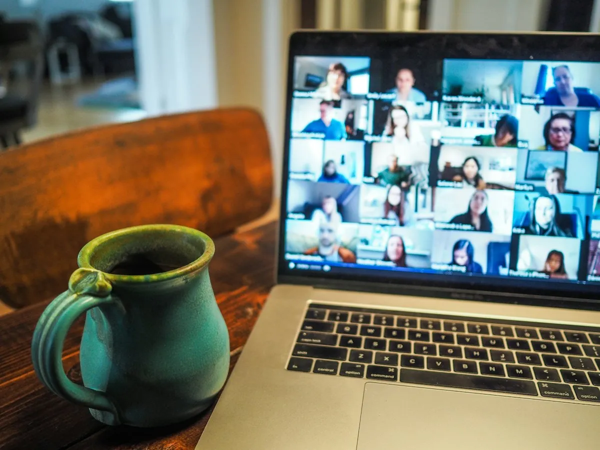 Laptop showing a video call with many participants next to a coffee mug