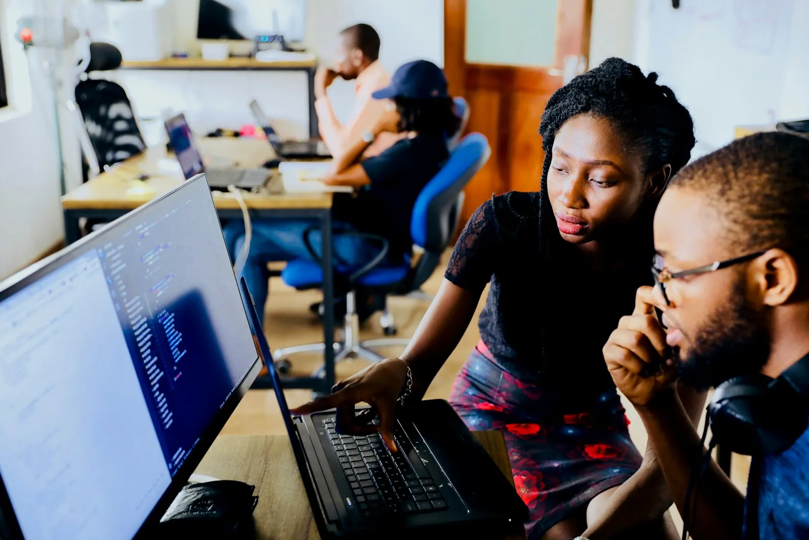 Two engineers discussing code on a monitor in a busy office